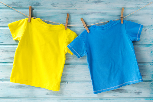 Two bright baby t-shirts hanging on a clothesline on a blue wooden background