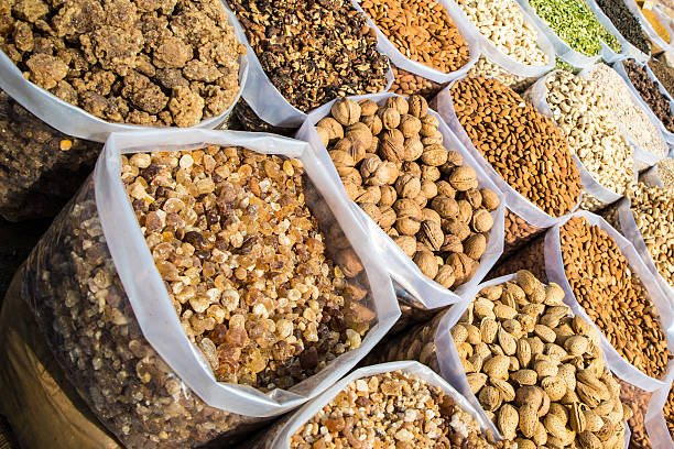 In India, a scene from one of Old Delhi's outdoor markets where big plastic bags filled with a variety of nuts such as walnuts, cashews, pinions and blanched or roasted almonds. are on the ground in cardboard boxes. Candied fruits and Spices are also visible in the image.