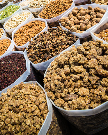 In India, a scene from one of Old Delhi's outdoor markets where big plastic bags filled with a variety of nuts such as walnuts, cashews, pinions and blanched or roasted almonds. are on the ground in cardboard boxes. Candied fruits and Spices are also visible in the image.