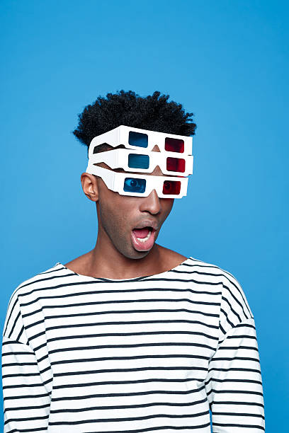 Surprised afro american guy wearing 3d glasses Surprised afro american young man wearing striped top and 3d glasses. Studio portrait, blue background. 3 d glasses stock pictures, royalty-free photos & images