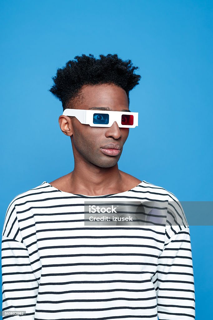 Afro american guy wearing 3d glasses Afro american young man wearing striped top and 3d glasses. Studio portrait, blue background. 3-D Glasses Stock Photo