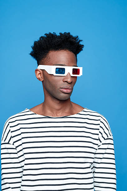 Afro american guy wearing 3d glasses Afro american young man wearing striped top and 3d glasses. Studio portrait, blue background. 3 d glasses stock pictures, royalty-free photos & images