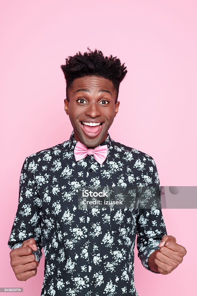 Successful afro american young man Portrait of excited afro american young man wearing floral pattern shirt and pink bow tie, laughing at camera. Studio shot, pink background. Portrait Stock Photo