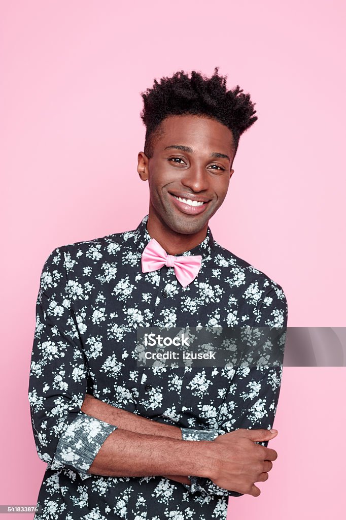 Friendly fashionable afro american young man Portrait of happy afro american young man wearing floral pattern shirt and pink bow tie, smiling at the camera. Studio shot, pink background. African Ethnicity Stock Photo