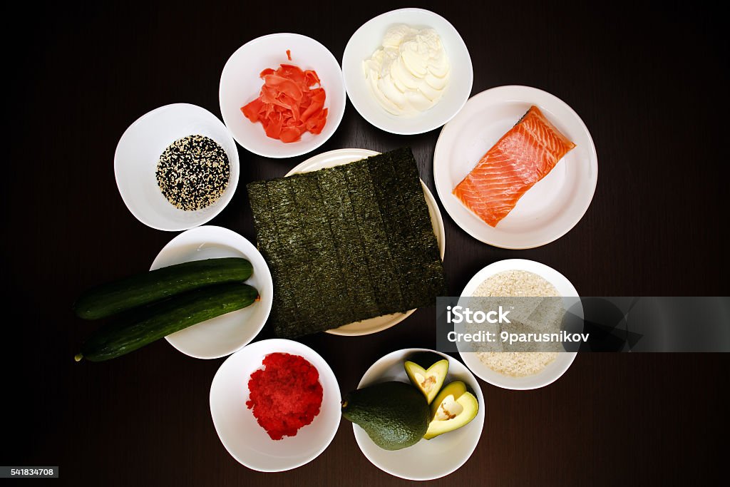 Table served with Ingredients of sushi and traditional japanese food Table served with Ingredients of sushi in plates on dark background. rice with vegetables, nigiri, soy sauce, cucumber, salmon, avocado, caviar, nori, sesame. Before to be a roll. Top view Agriculture Stock Photo