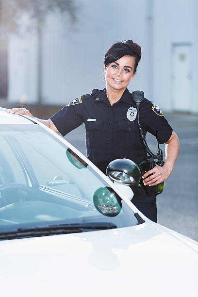 Female police officer standing next to patrol car A policewoman standing next to her patrol car, smiling and looking at the camera with one hand on her hip, and the other resting on the car. She is wearing the standard navy blue policeuniform. female police officer stock pictures, royalty-free photos & images