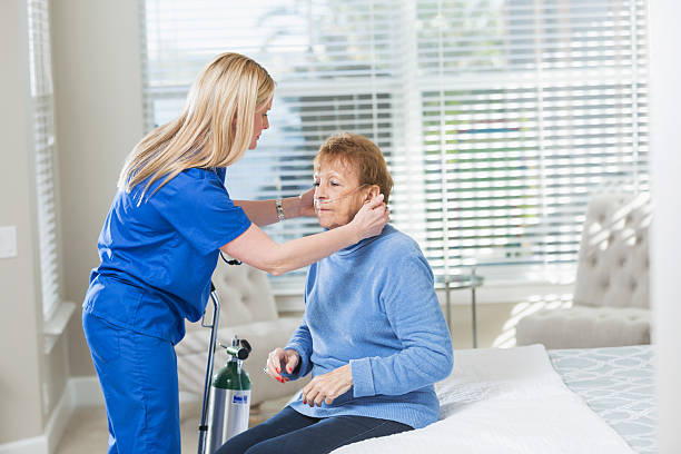 Home healthcare nurse helping elderly woman with oxygen Home healthcare worker helping a senior woman with her oxygen tank. They are in the woman's bedroom. The nurse is wearing blue scrubs. o2 stock pictures, royalty-free photos & images