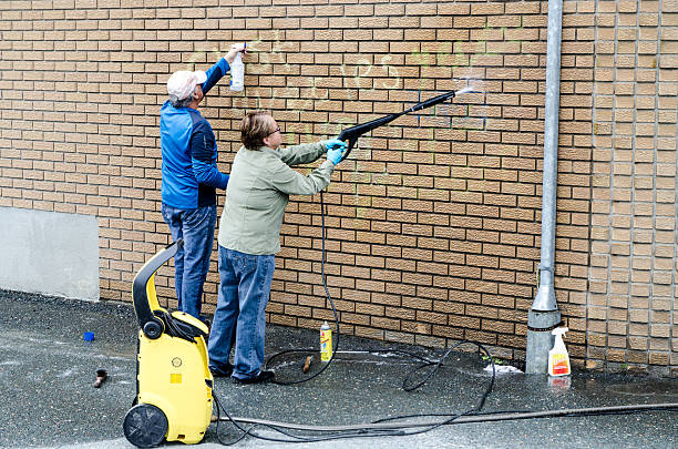 Man and woman cleaning graffiti on their brick wall Sherbrooke, Canada - June 11, 2016: Man and woman cleaning graffiti on their brick wall using brush, cleaner and pressure water hose during a day of springtime. sherbrooke quebec stock pictures, royalty-free photos & images