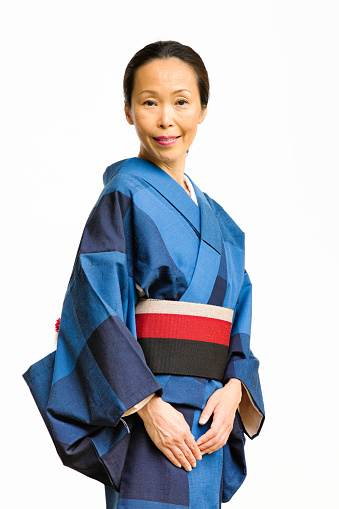 Smiling serene mature Japanese woman in kimono portrait in front of white background.