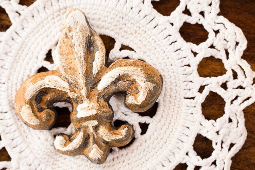 Close up view of a doiley and fleur de lis on wooden table.  Decor.  Full frame.