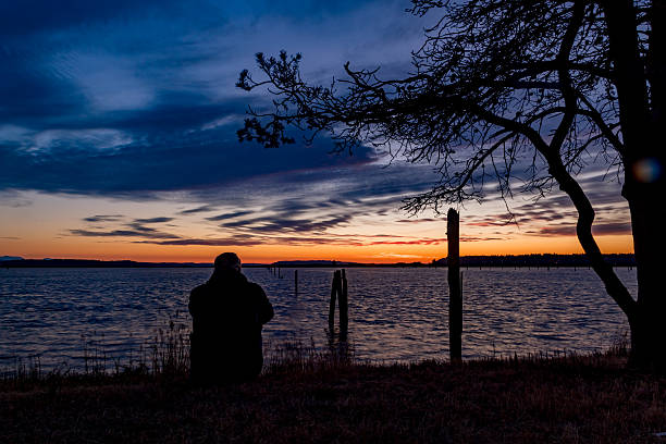 istock Man sitting on grassy shore at sunset 541851016