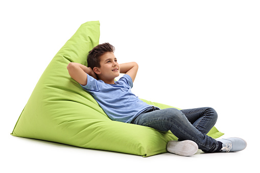Relaxed boy laying on a comfortable green beanbag isolated on white background