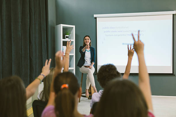 Kids Coding In School. Group of children at coding class. Teacher sitting and asking questions and children raising hands to answering. Teacher pointing on kids. teacher projector stock pictures, royalty-free photos & images