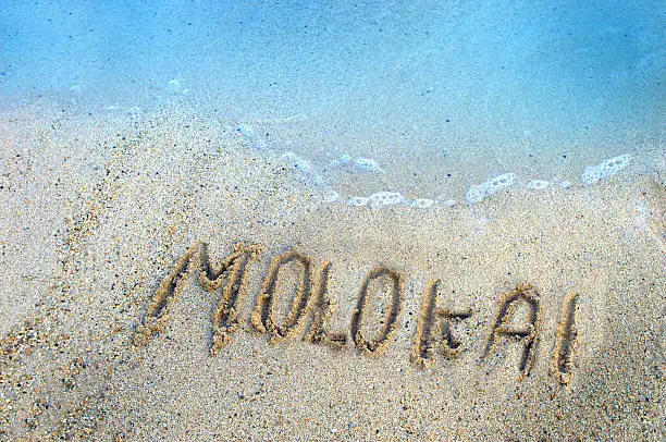 Finger drawn letters withstand the gentle ebb and flow of the aqua waters of the Pacific Ocean surrounding the Hawaiian Islands.  Molokaii holds its own in the coarse, salt and pepper sand of its shoreline.