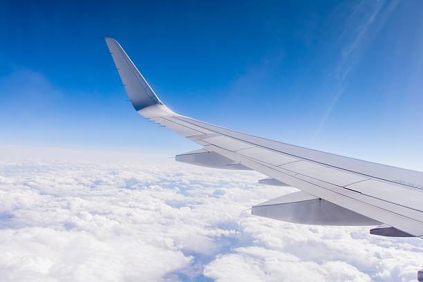 View of an Airplane Wing from Window Seat View of silver airplane wing from the window seat with blue sky and clouds. aircraft wing stock pictures, royalty-free photos & images