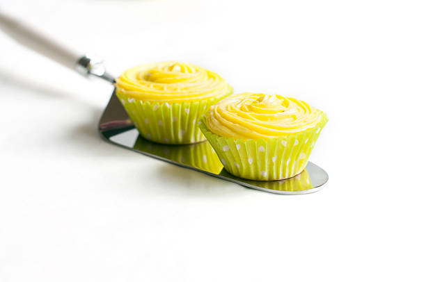Two cupcakes with yellow cream on cake shovel on white background. Selective focus