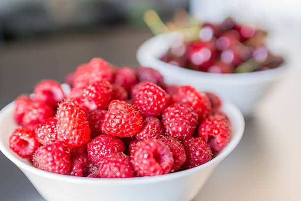 istock Raspberries in the white bowl with cherries in background 542007962