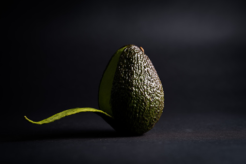 A single half peeled avocado on a black background.
