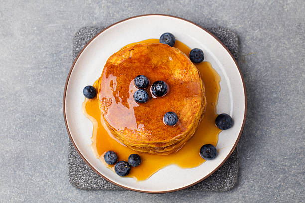 Pumpkin pancakes with maple syrup and blueberries. Top view Pumpkin pancakes with maple syrup and blueberries on a plate. Grey stone background Top view. winter food top view stock pictures, royalty-free photos & images
