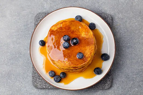 Pumpkin pancakes with maple syrup and blueberries on a plate. Grey stone background Top view.