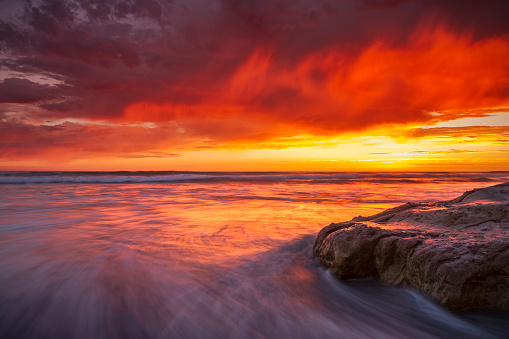 A fiery orange sunset reflects in the ocean waves on a beach in Del Mar, California.