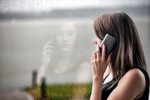 Woman looking stressed with technology , Bad news! , girl using smart phone and  sitting near window, Unwanted phone call, Depression - Sadness, Sadness, Window