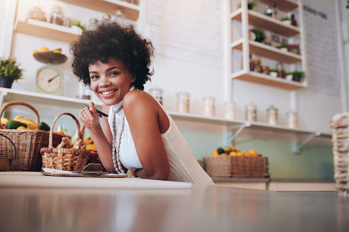 Portrait of smiling young woman working in a juice bar. African female standing behind the counter looking at camera and smiling.