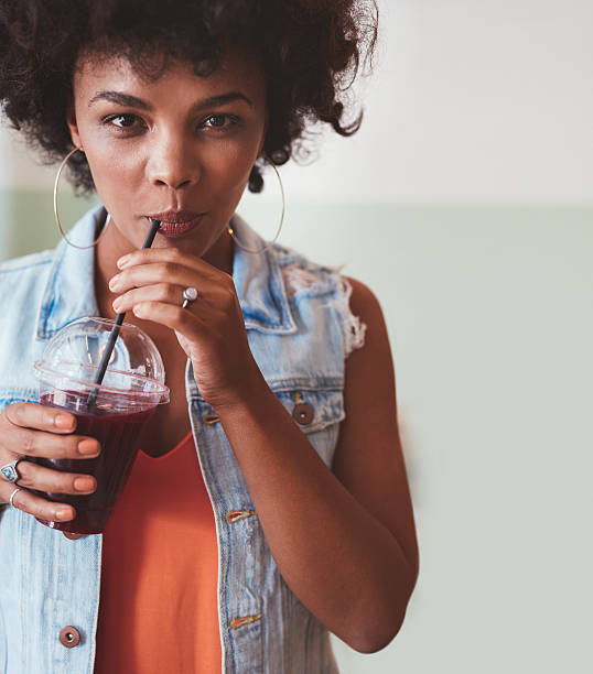 Close up shot of an attractive young woman drinking juice. Stylish african female model getting some refreshment.