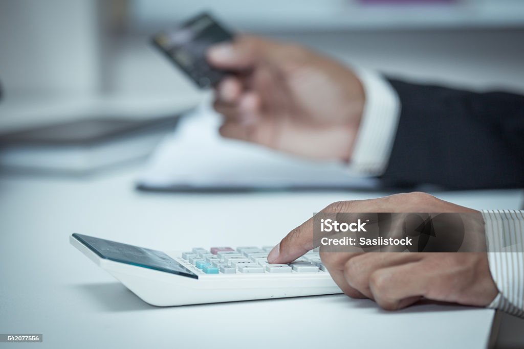 Businessman using a calculator to calculate his payment on credi Businessman using a calculator to calculate his payment on creditcard in vintage color filter ATM Stock Photo