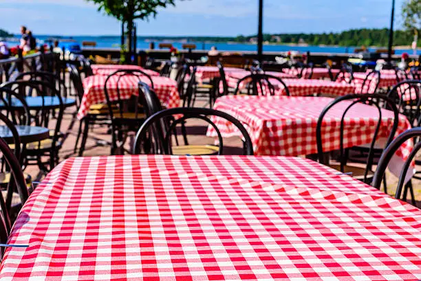 Red and white checkered table cloths at an outdoor eatery with coastline in background. Copy space on cloth.