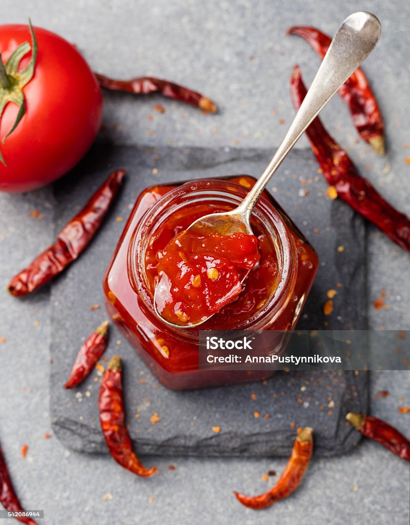 Tomato and chili sauce, jam, confiture in a glass jar Tomato and chili sauce, jam, confiture in a glass jar on a grey stone background Top view. American Culture Stock Photo