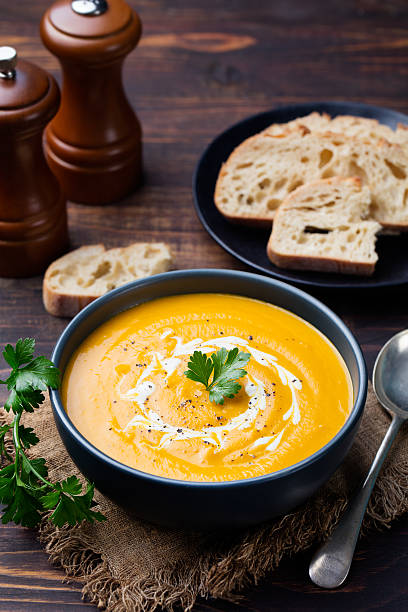 Pumpkin and carrot soup with cream and parsley Pumpkin and carrot soup with cream and parsley on dark wooden background. pumpkin soup photos stock pictures, royalty-free photos & images