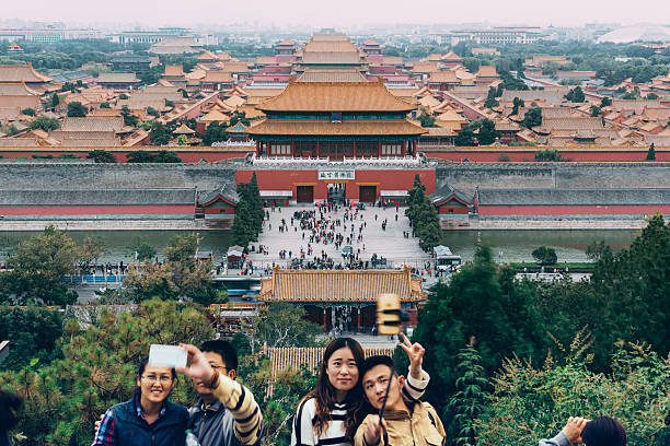 Beijing, China-October 2019; Large group of tourists seen from the back listening to a tour guide with in the back the Hall of Central Harmony