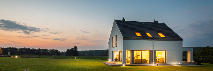 Panoramic photo of modern house with outdoor and indoor lighting, at night