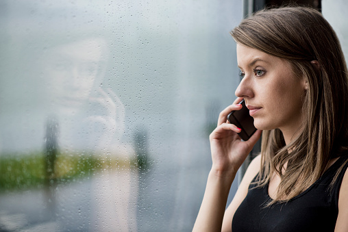 Woman looking stressed with technology , Bad news! , girl using smart phone and  sitting near window, Unwanted phone call, Depression - Sadness, Sadness, Window