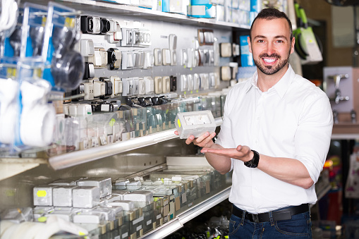 young glad european man picking electric plug in household shop