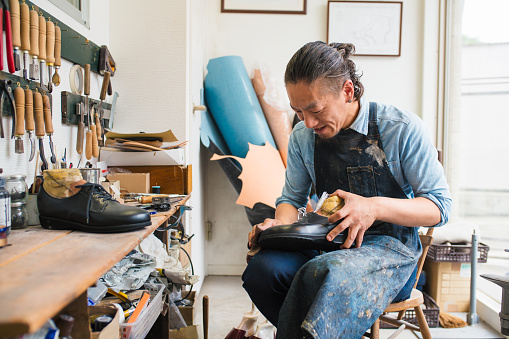 Craftsperson sat repairing or making a pair of leather shoes in his workshop. Kyoto, Japan. May 2016