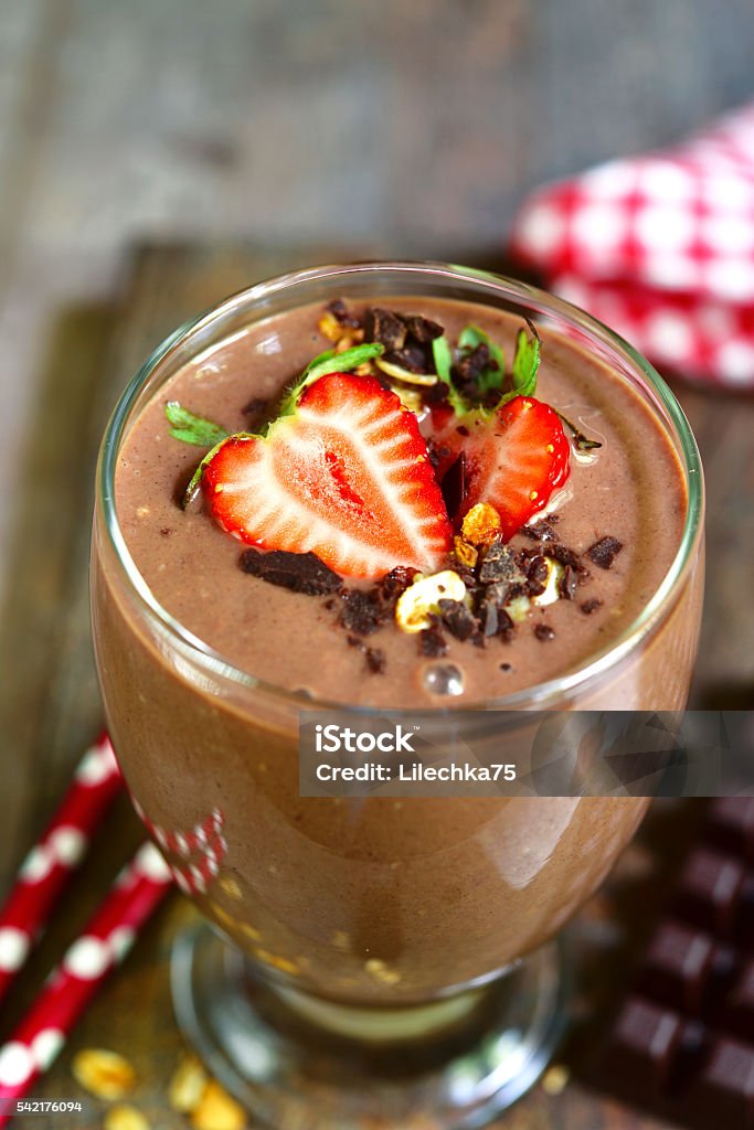 Chocolate banana smoothie with strawberry. Chocolate banana smoothie with strawberry in a glass on a rustic wooden background. Banana Stock Photo
