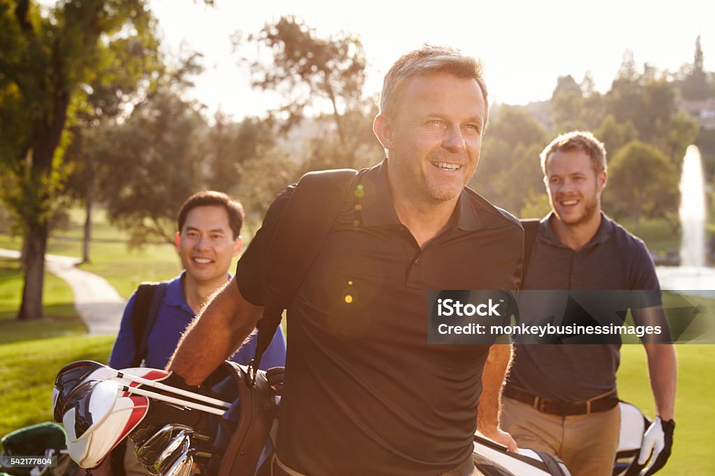 Grupo de jogadores de golfe masculinos caminhando ao longo da passarela Carregando sacos - Foto de stock de Golfe royalty-free