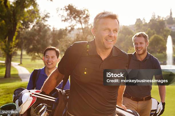 Foto de Grupo De Jogadores De Golfe Masculinos Caminhando Ao Longo Da Passarela Carregando Sacos e mais fotos de stock de Golfe