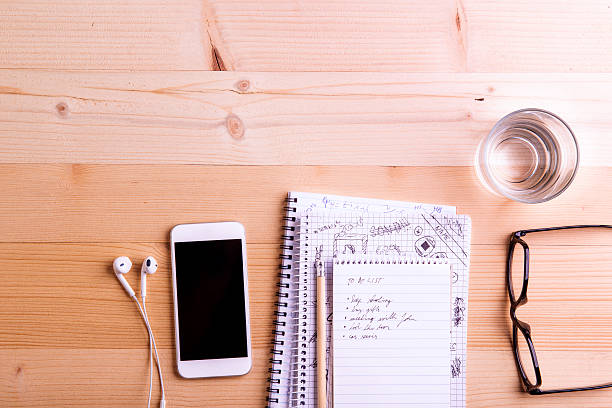 Smartphone, earphones, glass of water and eyeglasses laid on office desk. Desk with gadgets and office supplies. Studio shot on wooden background. Flat lay, empty copy space.