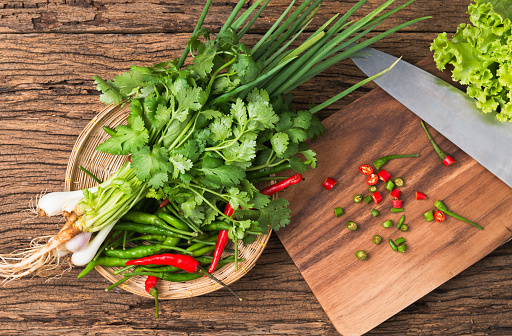 fresh spring onion, coriander and chili on basket on wooden background