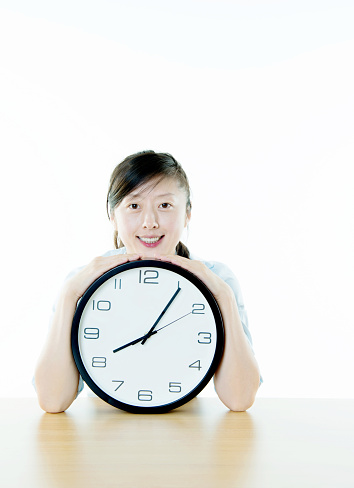 Young woman holding a wall clock against white background.