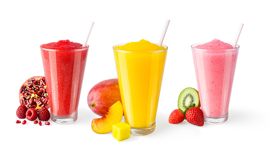 Three flavors of cold fruit smoothies are in generic glasses with straws on a white background. Fresh fruits as garnishes are sitting next to each glass. From left to right, the frosty blends are: pomegranate raspberry (red), peach mango (yellow), and kiwi strawberry (pink). These could be non-alcoholic smoothies or frozen cocktails.