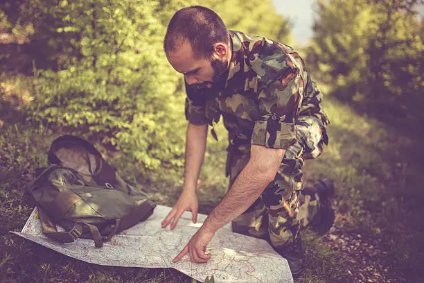 War, army and people concept - young soldier or ranger wearing military uniform ,looking at the map