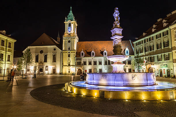 Bratislava, Slovakia - April 29, 2016: Old Town Hall in Bratislava, Slovakia at night with part of Maximilians Fountain in the foreground. People can be seen.