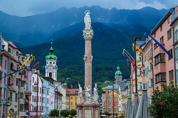 A view along Maria-Theresien-Strasse in Innsbruck during the day. The Annasaule column and the outside of buildings can be seen and mountains can be seen in the distance.