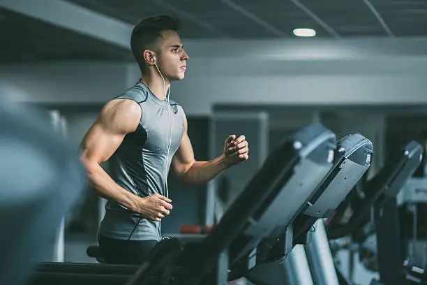 Young man in sportswear running on treadmill at gym