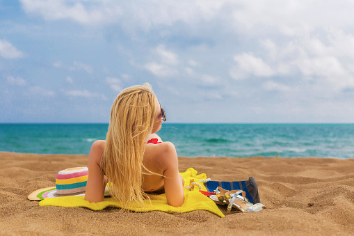 Rear view of woman in bikini relaxing on beach towel enjoying the sea view