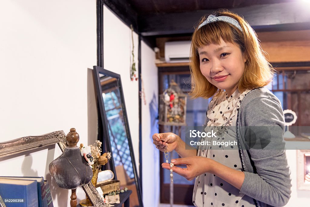 Japanese Woman Working in Her Own Business Selling Jewelry This is a horizontal, color photograph of a stylish Japanese woman working in her small business, a boutique shop selling vintage items and accessories in Kyoto, Japan. Smiling, she holds up a necklace for sale. Photographed with a Nikon D800 DSLR camera. 30-39 Years Stock Photo